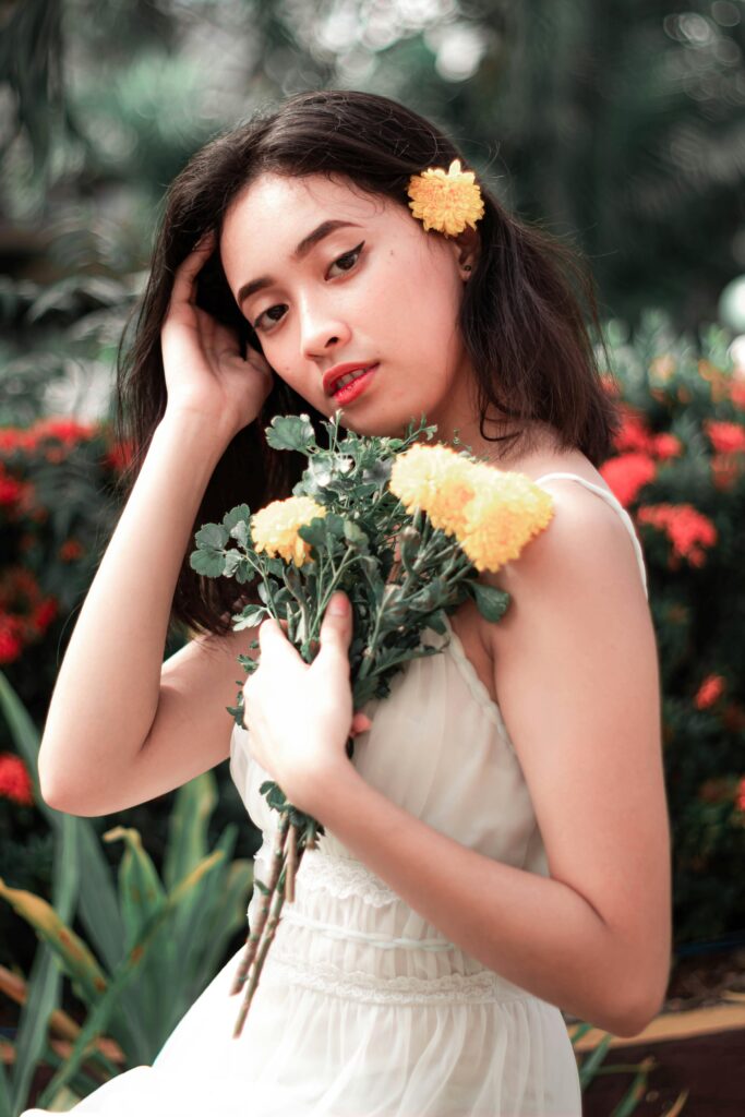 Woman in a light cream sleeveless dress holding yellow flowers, styled as a spring wedding guest dress with floral elegance.
